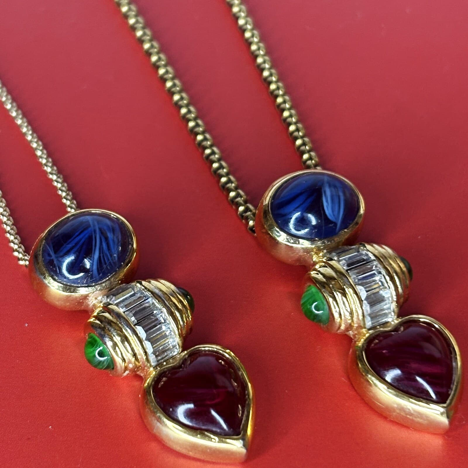 A pair of vintage Dior earrings repurposed into pendants — carved cobalt-blue glass cabochons, clear baguette crystals and deep red glass hearts in gold settings, each hung on a gold chain