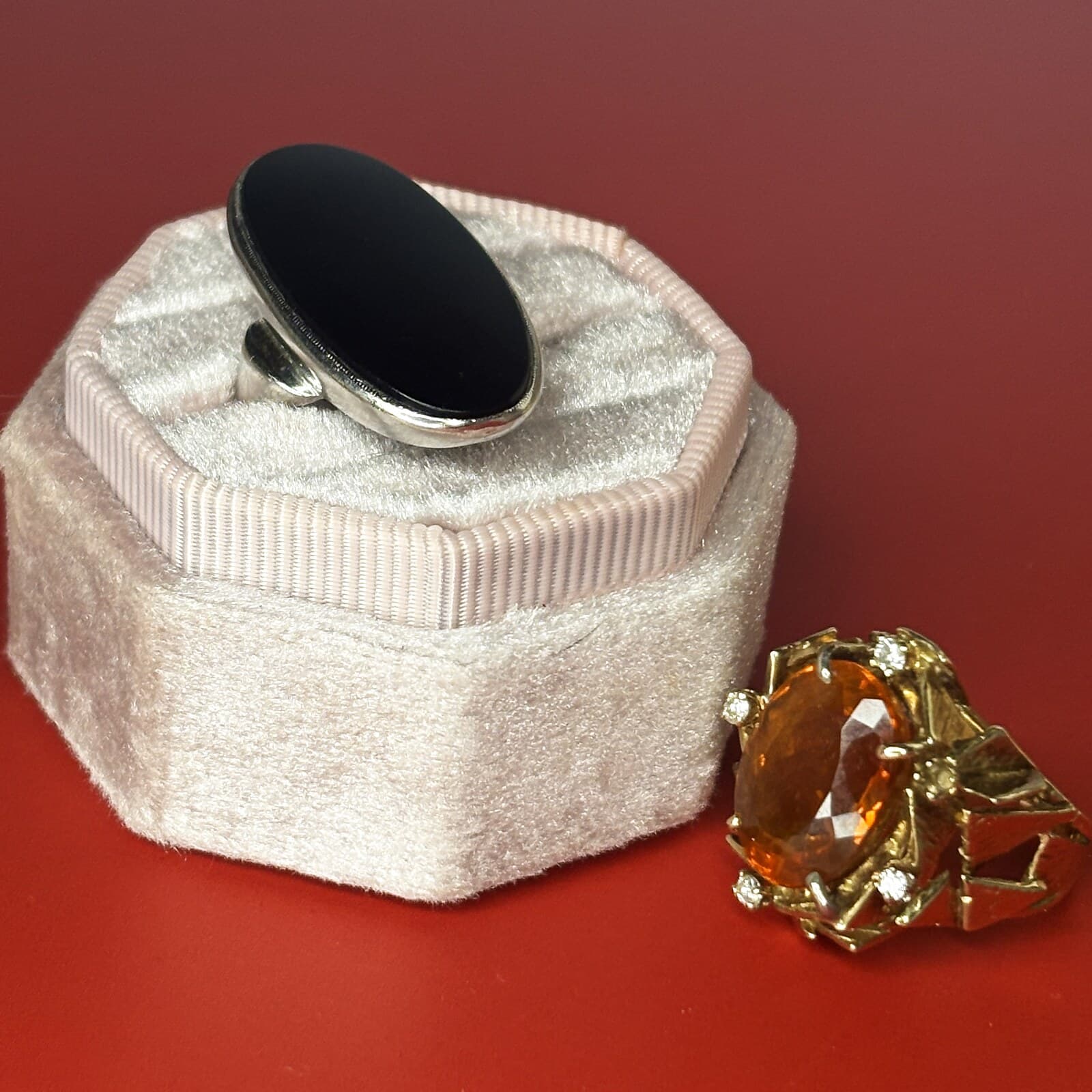Handed-down rings — an oval black onyx ring in a silver bezel resting on a blush velvet ring box, beside a gold cocktail ring set with a faceted orange citrine